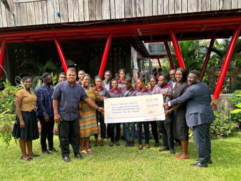 DEI-and-Fidelity-Bank-staff-stand-together-holding-a-dummy-cheque-with-the-beneficiary-students.-1